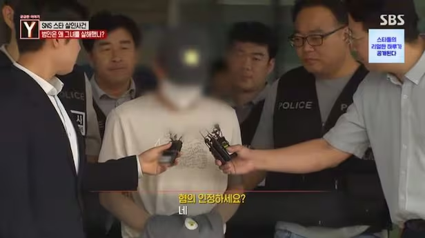 Choi, the man known online as "Black Cat," is escorted by police officers following his arrest in September 2024. When asked by reporters if he admitted to the charges, he answered: "Yes." SBS broadcast. Credit: The Chosun Daily.