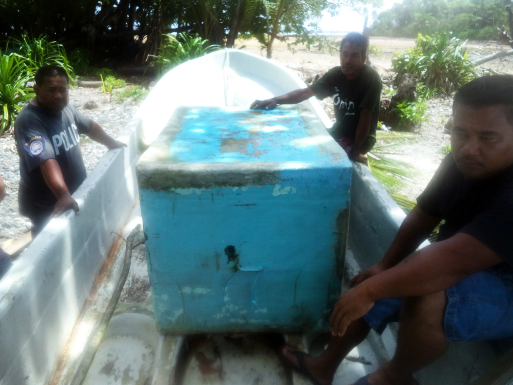 Three men inspect a fibreglass dinghy on a Pacific shoreline. Fibreglass boats replaced traditional dugout canoes across Melanesia within a single generation from the 1970s onward.