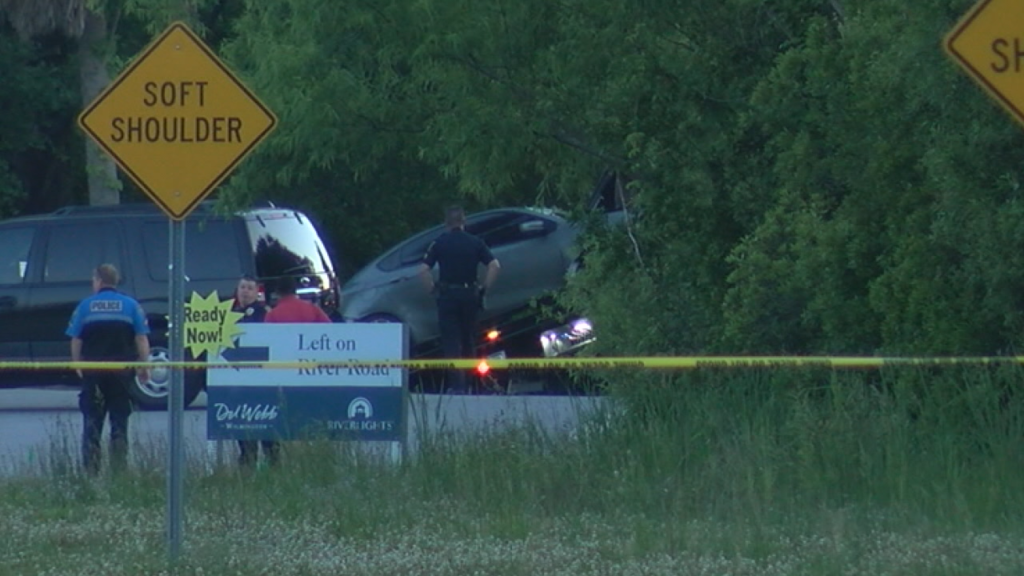 Stephanie Mayorga and Paige Escalera Disappeared in Seconds. Their Car Sat in the Woods for Nineteen Days. 3 Wilmington Police Department officers secure the scene at the intersection of River Road and Independence Boulevard, Wilmington, North Carolina, on May 4, 2020, after Paige Escalera's grey 2013 Dodge Dart was recovered deep in the tree line. The signage visible at the intersection marks the same stop the car failed to stop at nineteen days earlier.