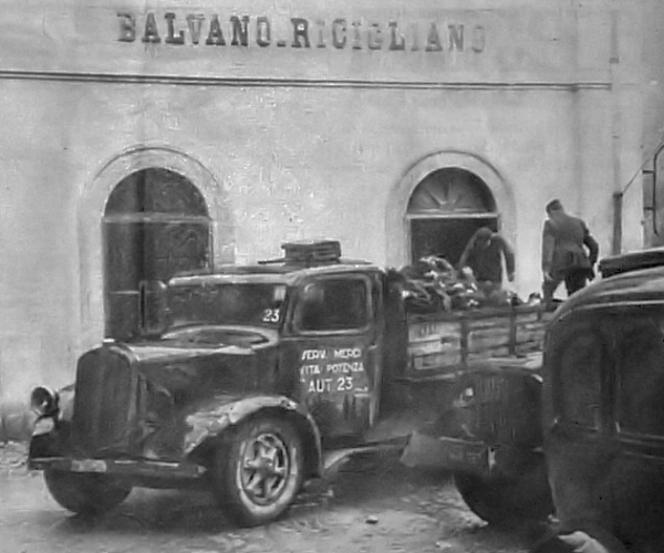 A truck marked "Servizio Medico Vita, Potenza" loads bodies at Balvano-Ricigliano station for transport to the common grave.