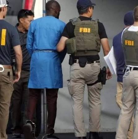 How Oluwadamilola Bamigboye Shouted "Drive" in a Plymouth Parking Lot, Trapped a Federal Agent in a Moving Jeep at Gunpoint, and Ended Up in Federal Court 5 FBI agents escort a handcuffed suspect into federal custody following the December 2025 Plymouth, Minnesota incident in which Oluwadamilola Bamigboye and Rekeya Frazier were charged with assaulting a Homeland Security Investigations agent.